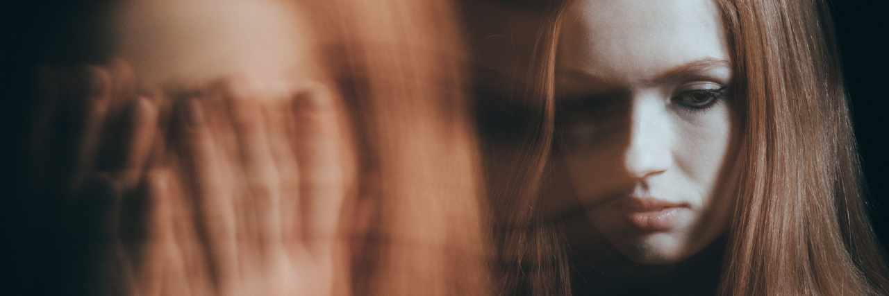 When Anxiety Makes You a Living Paradox Stressed, young woman covering her face, dark background