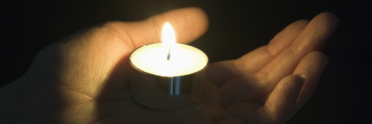 person's hand holding a tea light candle