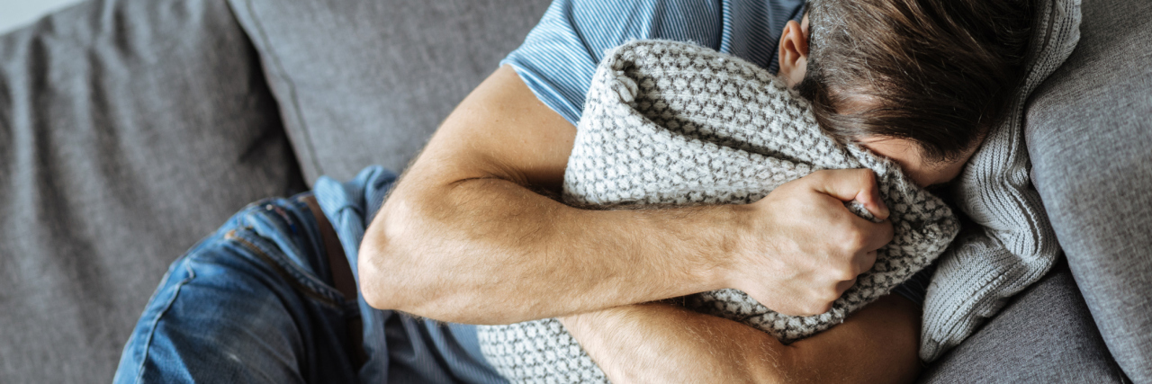 What It's Like to Be Male and Triggered by Sexual Abuse upset man lying on sofa hugging pillow crying