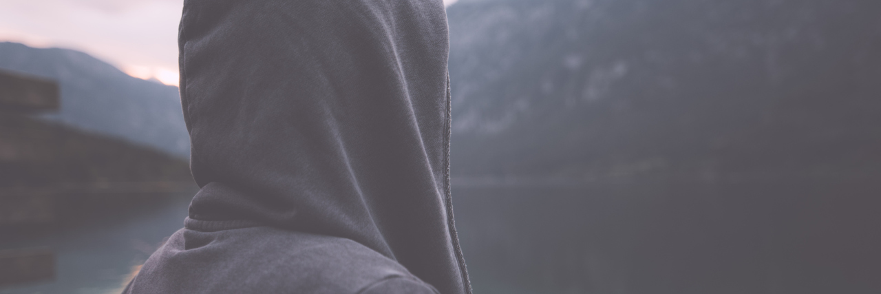 woman wearing a hoodie and standing outside near a lake