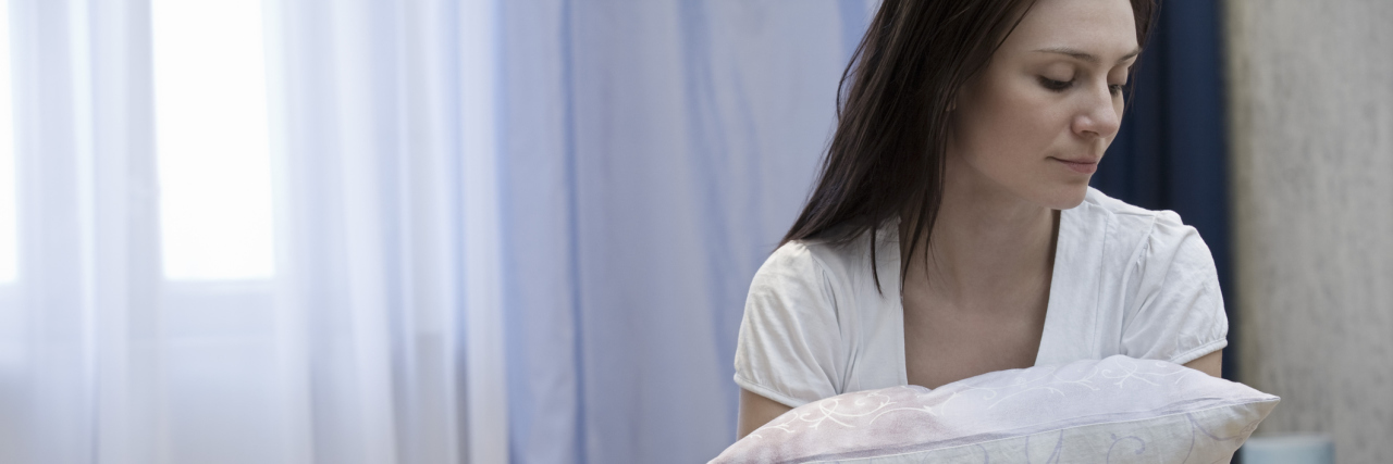 Asthma: The Importance of Listening to Your Body With Chronic Illness Woman sitting on bed and hugging pillow