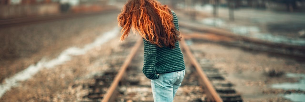 redhead woman standing on train tracks looking contemplative