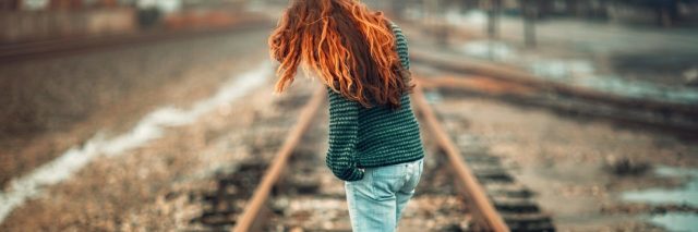 redhead woman standing on train tracks looking contemplative