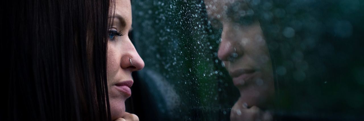 woman with dark hair looking out of rainy window and reflection