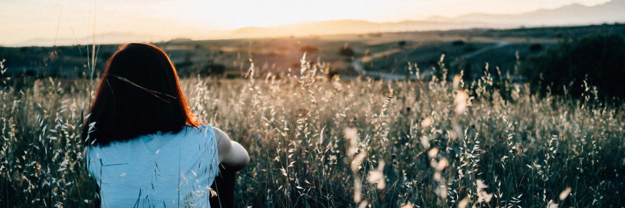 When Anxiety Pushes Your Friends Away young woman sitting among flowers and grass watching sunrise alone