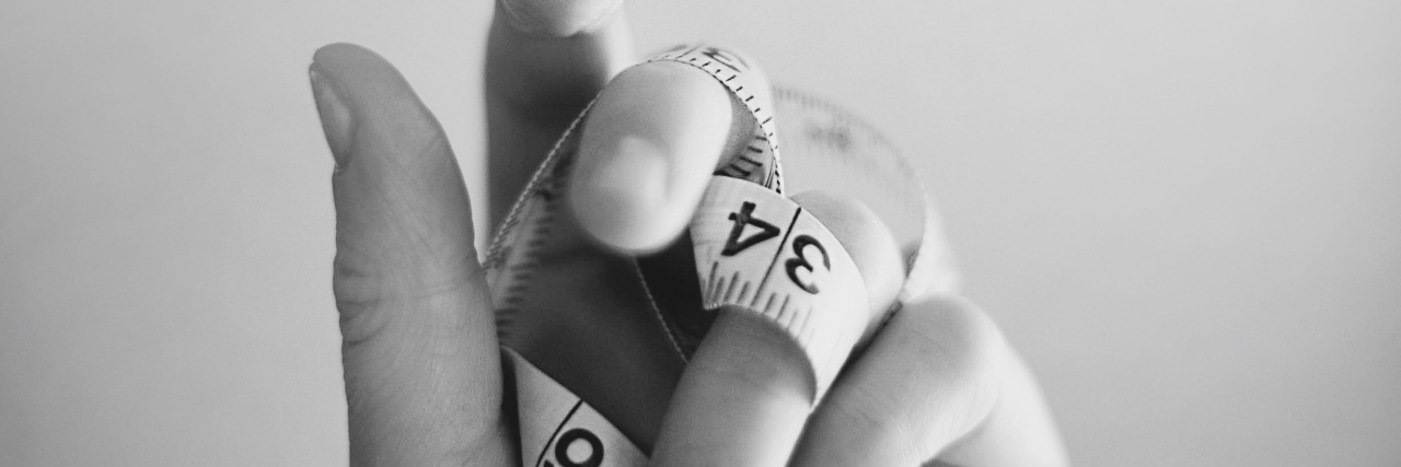 Gaining and Losing Weight Due to Chronic Illnesses Like Gastroparesis black and white photo of woman holding a tape measure