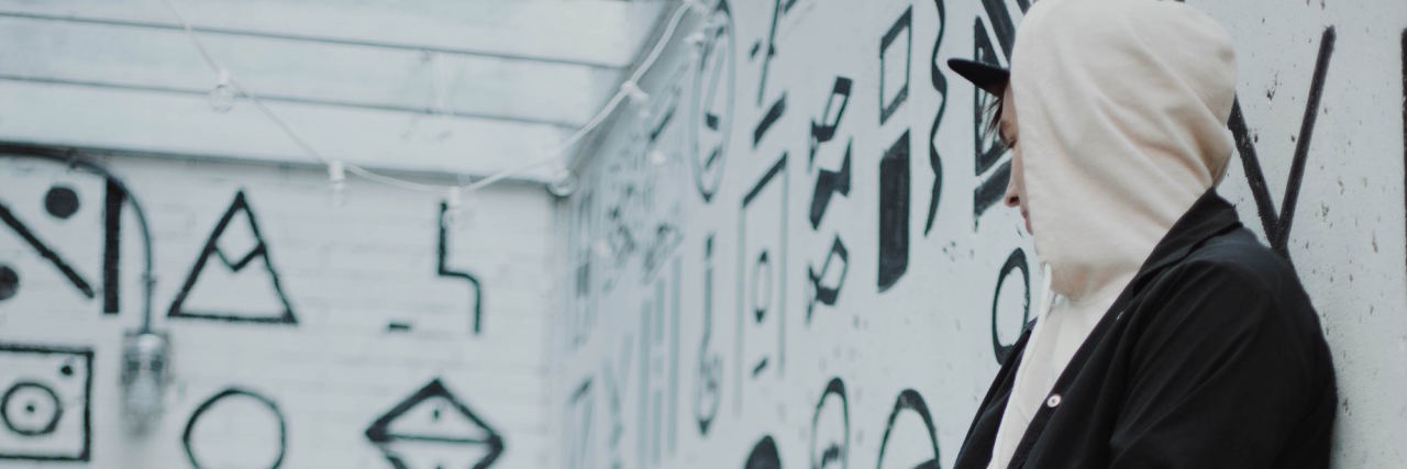 What People Don't Understand About Being a Male Rape Survivor man in a hoodie sitting in a white room with black drawn graphics on the wall, looking away