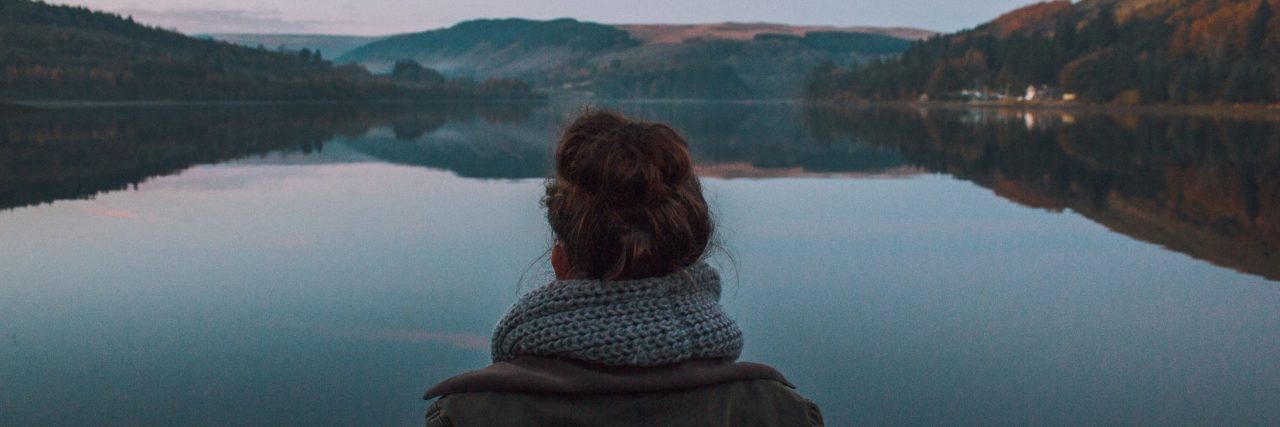 What Silence Means for a Person With Mental Illness woman standing alone in front of still lake surrounded by mountains