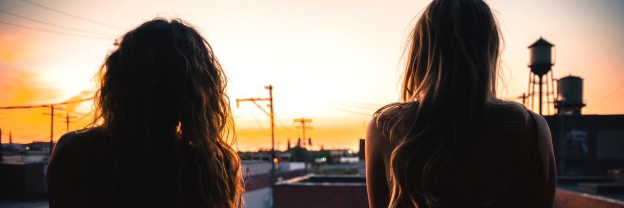 two young women watching sunset together back view
