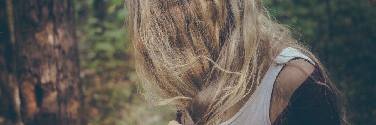 blonde woman with hair hiding face in woods looking anxious or upset