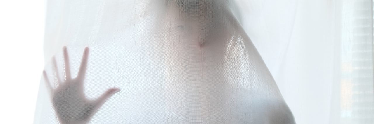 How My Mental Health Breakdown Saved My Life woman stands behind curtain with hand pressed to curtain