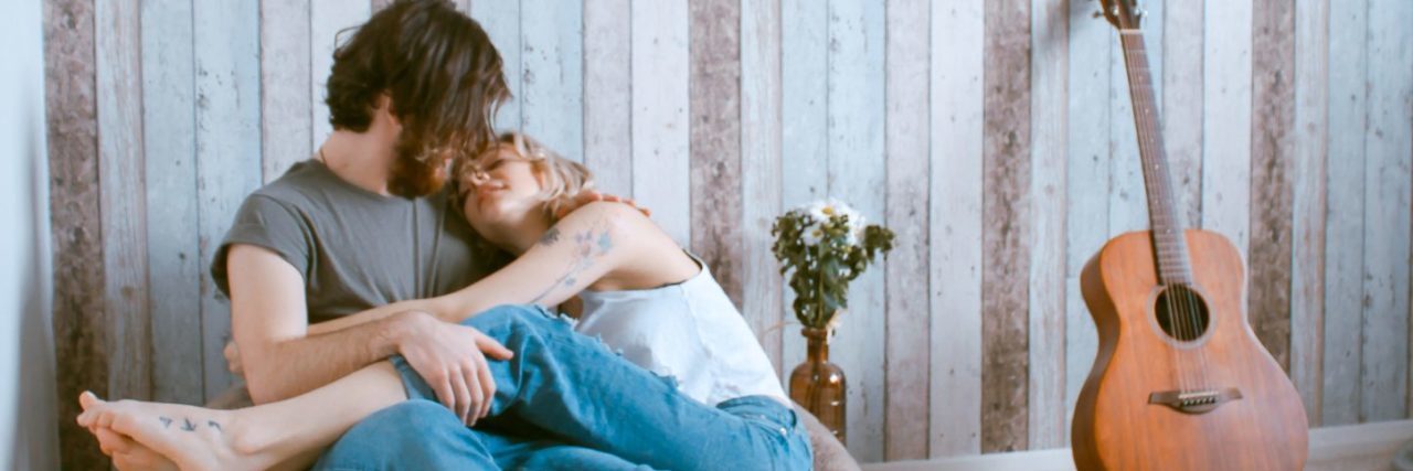 man and woman cuddled on bean bag next to acoustic guitar