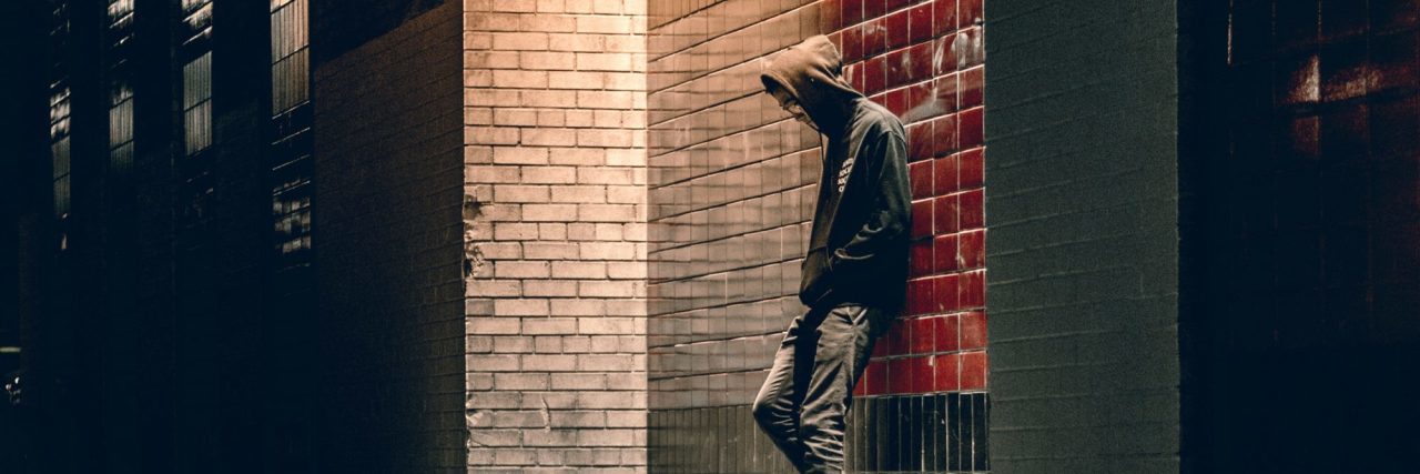 man standing alone against wall on dark street