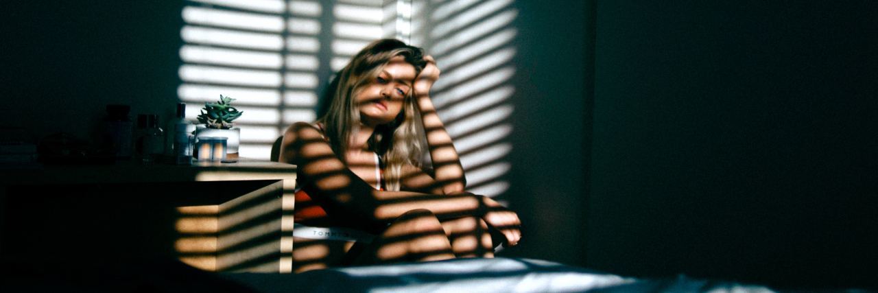 woman sits in the corner of the room with the blinds reflecting off of her