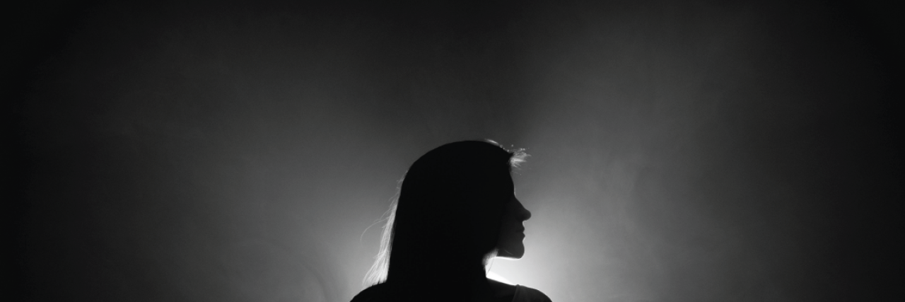 woman stands in dark with light shining behind her