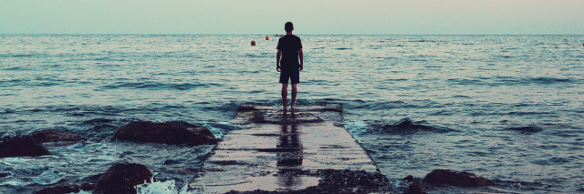 man stands at the end of a dock surrounded by water and the sunset