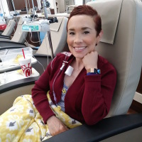 A photo of the writer sitting in a chemo chair.