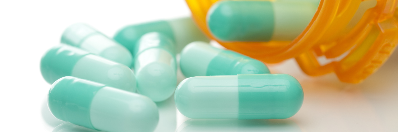 Prescription medicine pills pouring out of orange bottle. White background with reflective surface.