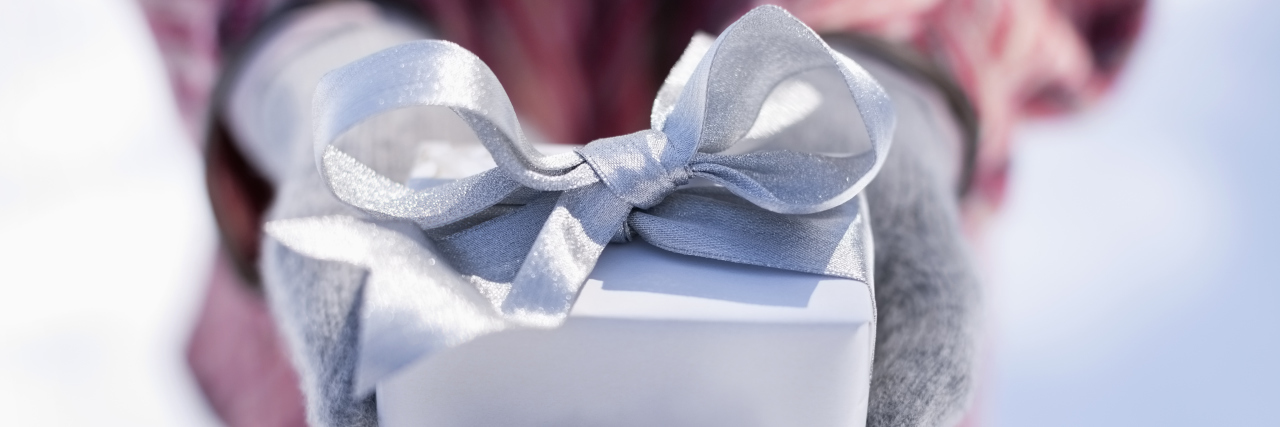 Fibromyalgia Gift Ideas and Products to Avoid woman wearing gloves outside in the snow and holding a silver wrapped present