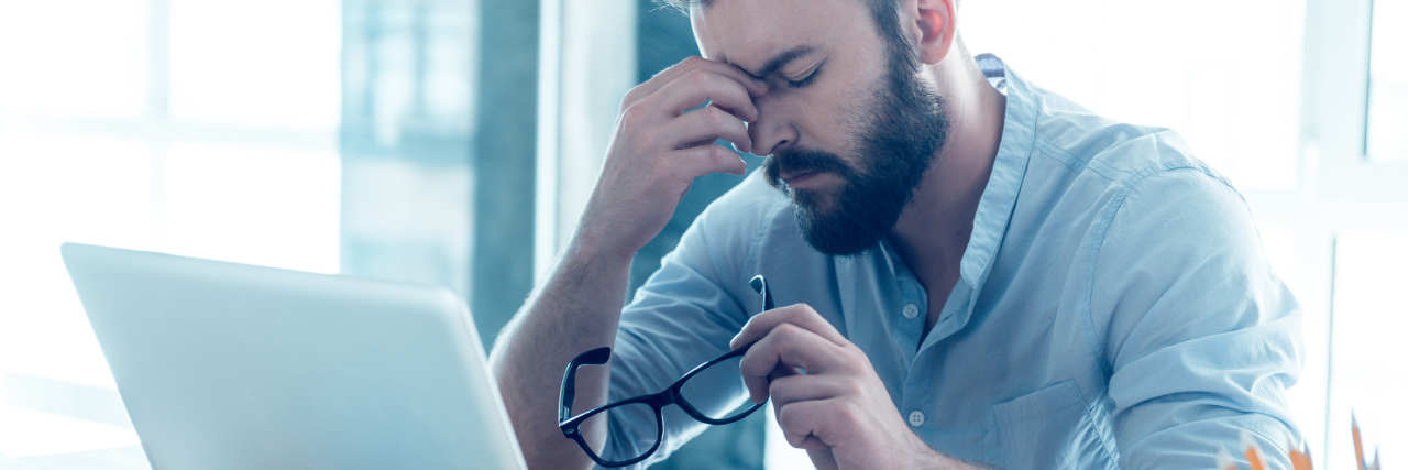 frustrated upset young man with beard in front of laptop pinching bridge of nose