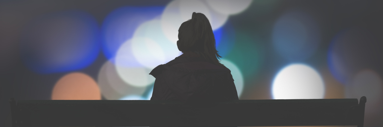 What You Should Remember Before You Judge Someone With MS A silhouette of a woman sitting on a bench, in front of city lights.