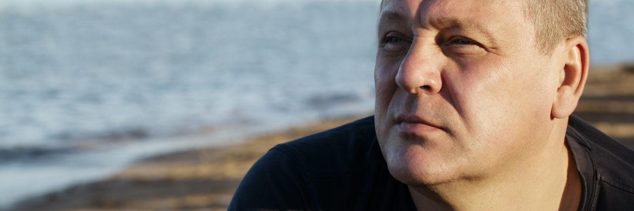 What Turning 55 With Borderline Personality Disorder Was Like Handsome middle-aged man sitting thinking in the sunlight at the coast with a serious expression and ocean backdrop