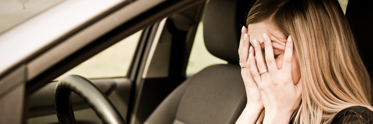 Young woman with hands on eyes sitting stressed in car.
