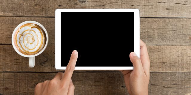 Fun and Creative Apps to Try When Your Pain Is Overwhelming Someone holding an iPad or similar device, with a cup of coffee next to them.