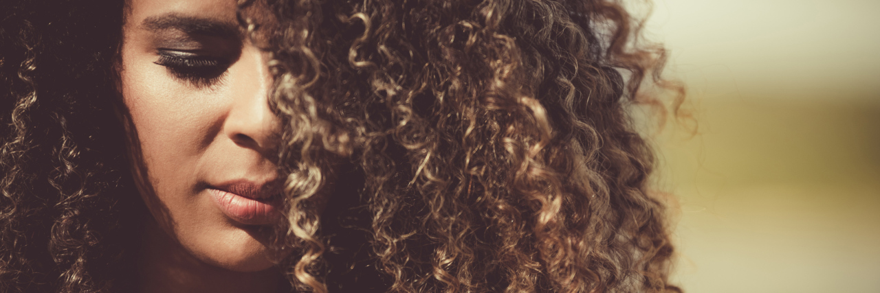 A close-up of an African American woman with curly hair, looking towards the ground.