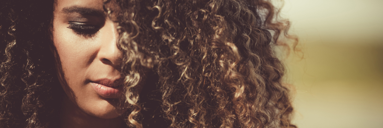 When Your Chronically Ill Friend Doesn't Meet Your Expectations A close-up of an African American woman with curly hair, looking towards the ground.