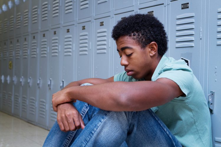 unhappy upset black teenager male sitting against school lockers