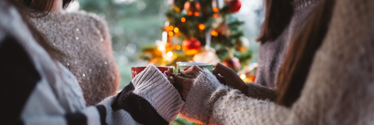 Tips for Anyone Struggling With an Eating Disorder During the Holidays Friend celebrating together and holding cups of warm tea. Christmas tree in background.