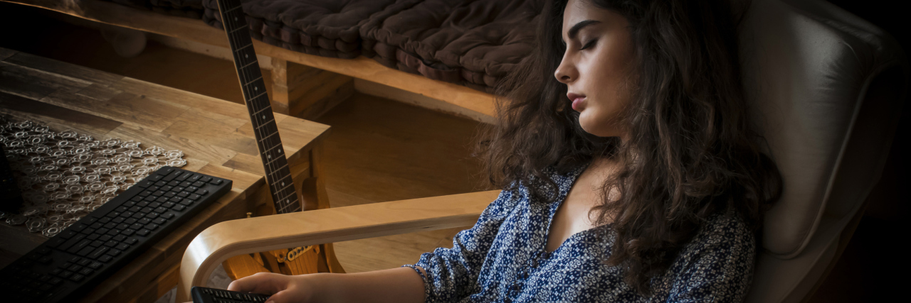 How My Mental and Physical Illnesses Make Me Tired A woman who fell asleep in her chair holding the TV remote.