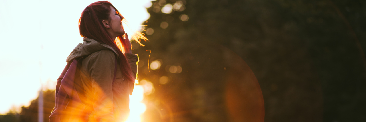 Smiling Young Red-haired woman dressed in jacket is enjoying vivid sunset in the streets.