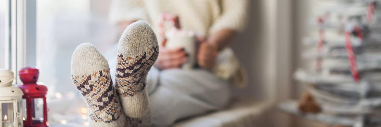 A Self-Care Checklist for Surviving the Holidays Young beautiful woman relaxing on window sill in christmas decorated home. Focus on foot