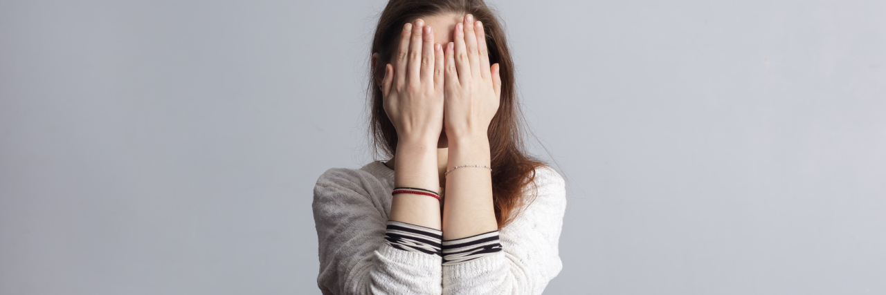 woman shame covering face with hands against plain background