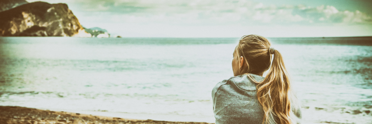 Moving Beyond Self-Doubt as a Person With Epilepsy Woman sitting on beach hugging her knees and looking into the distance with hope.