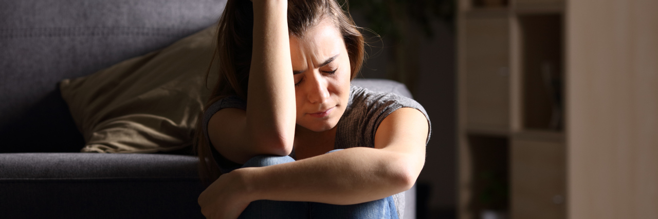 5 Ways to Move On From a Breakup Caused By Your Mental Illness Front view of a single sad teen sitting on the floor in the living room at home with a dark background