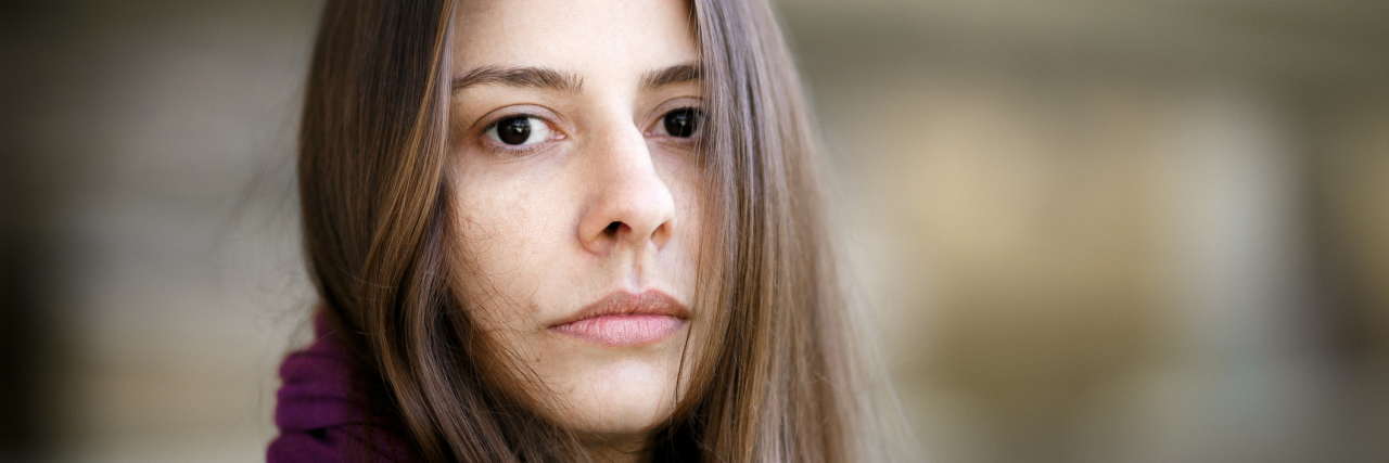 Why I'm Choosing to Be Realistic About My Chronic Illness A woman with a serious expression, looking at the camera.