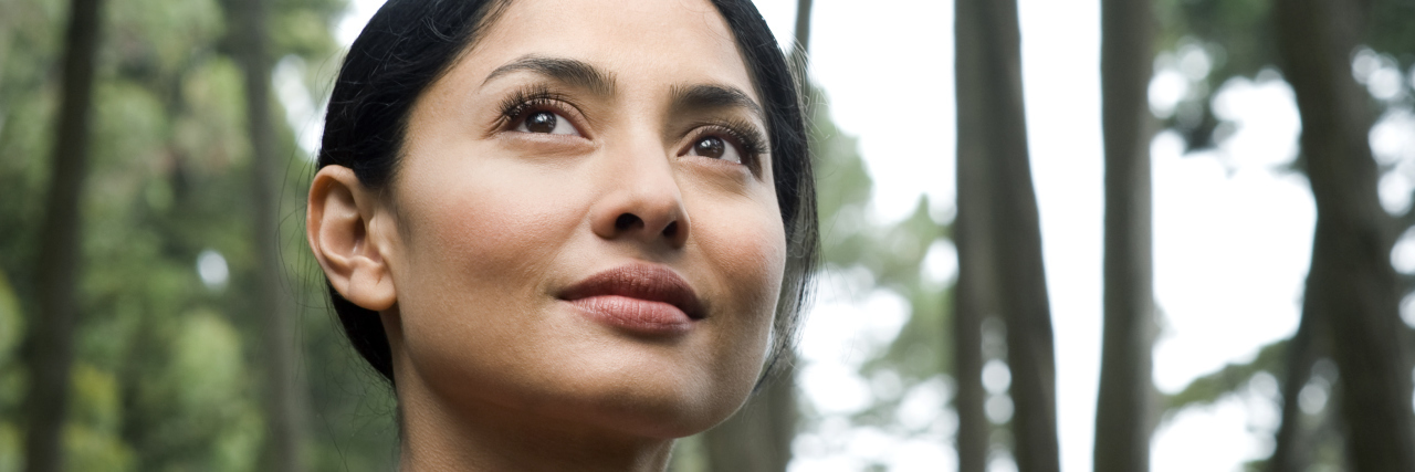 The Positives I Have Gained From Having Meniere's Disease woman standing outside in a forest looking up