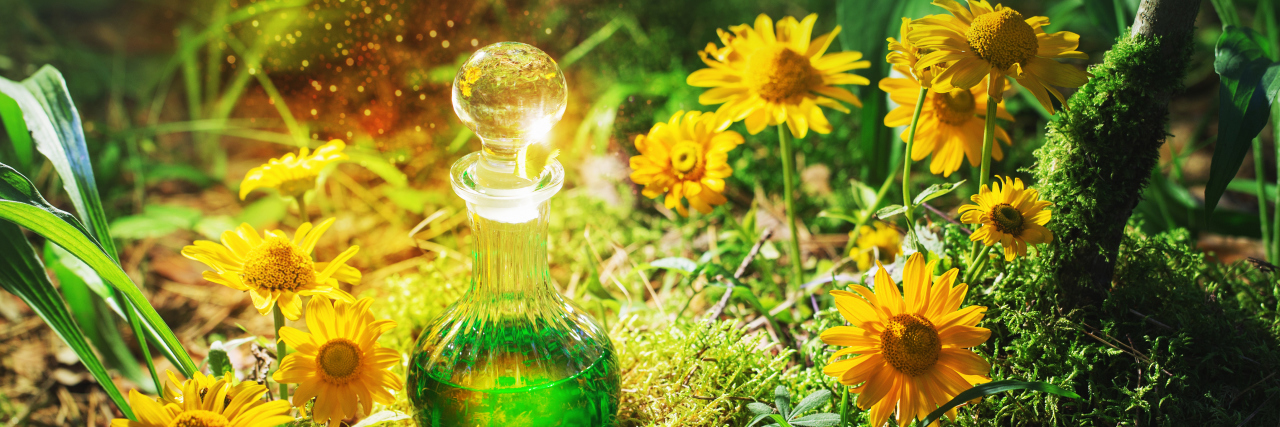 Why I Don't Want to Hear About 'Natural Cures' for My Illness A bottle filled with green liquid, sitting in some grass, surrounded by yellow flowers with the sun shining down on it.
