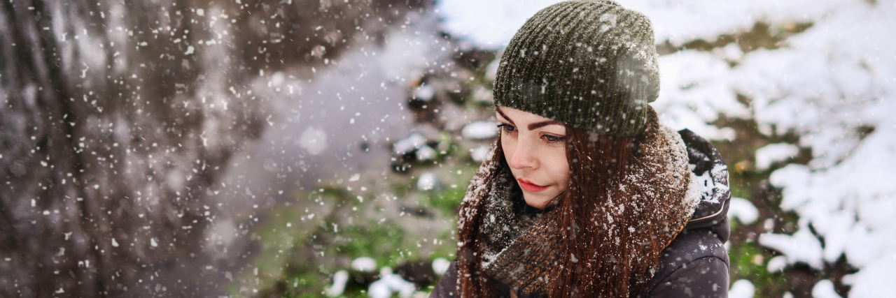 Why My Health Comes First This Christmas A downward image of a woman standing out in the snow, with a serious facial expression.