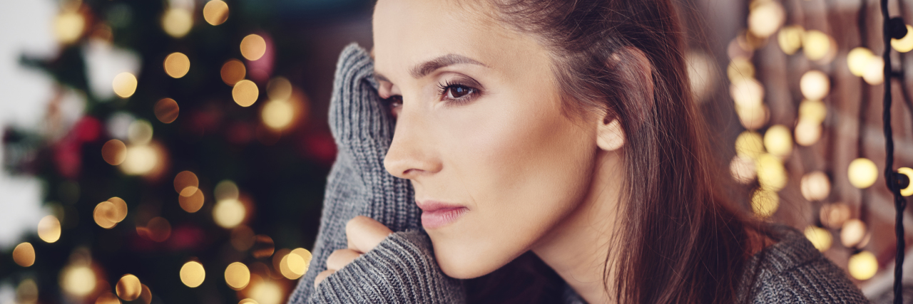 5 Ways I Deal With Seasonal Affective Disorder During the Holidays woman looking sad in front of a christmas tree