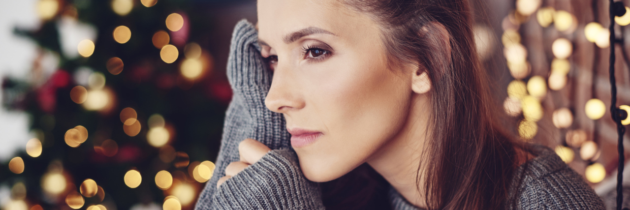 How Depression and Anxiety Affect Christmas Spirit woman at Christmas looking upset and pensive with tree in background