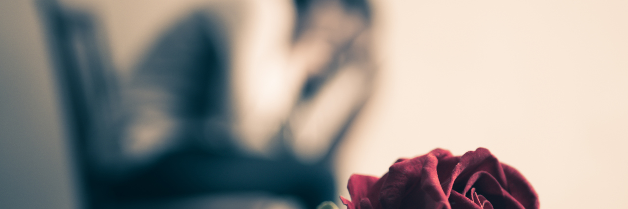 Retro sad woman sitting and crying with red rose in focus. Lonly , love, emotion concept.