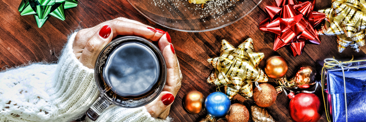 Woman holding a cup of tea, surrounded by holiday ornaments.