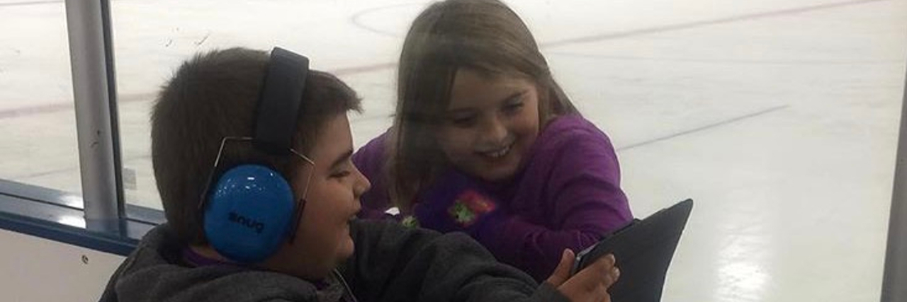 Boy wearing headphones showing a girl something on a tablet while at the skating rink.