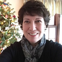 woman with short dark hair taking a selfie in front of a christmas tree