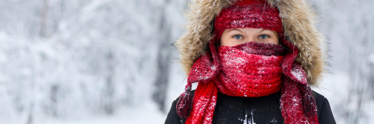 woman stands with scarf and hood over face during the winter