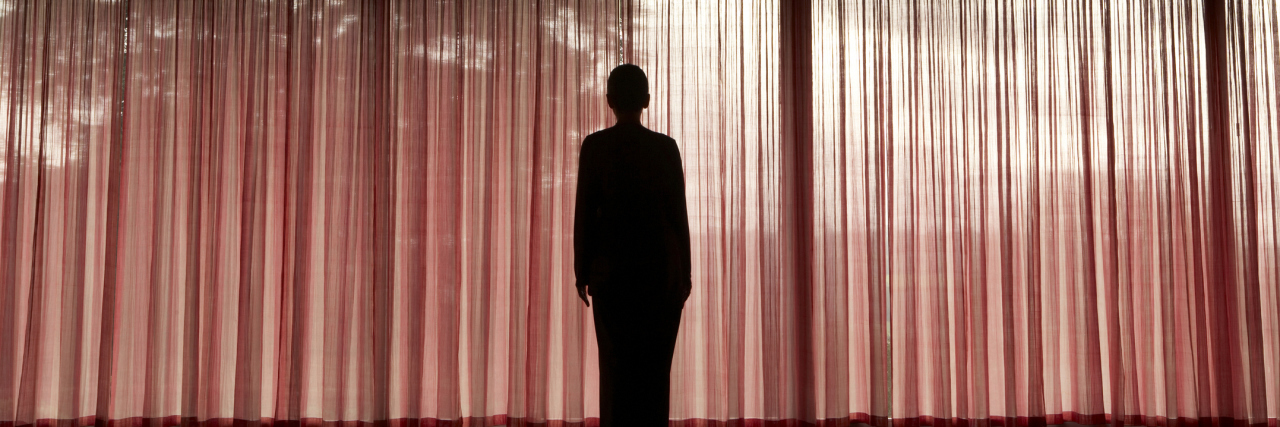 Mature woman standing in silhouette against red curtains